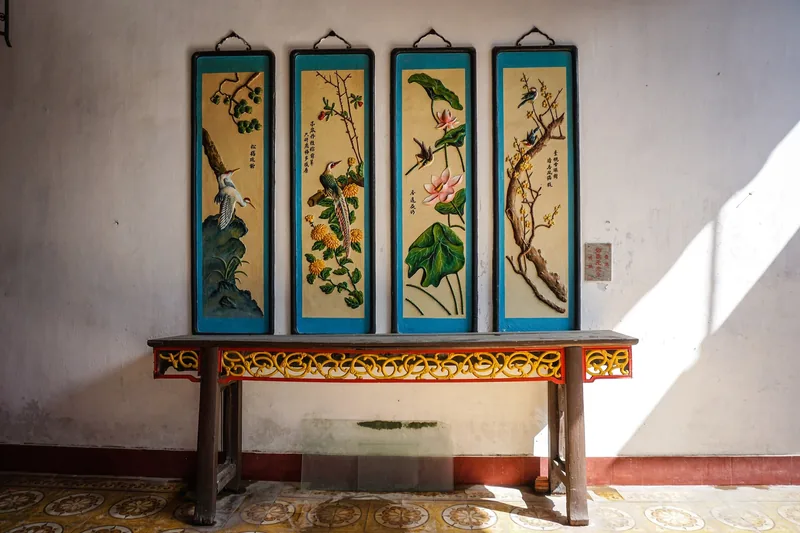 Four decorative bird and flower panels hang above a carved wooden altar table in a Hoi An heritage house.