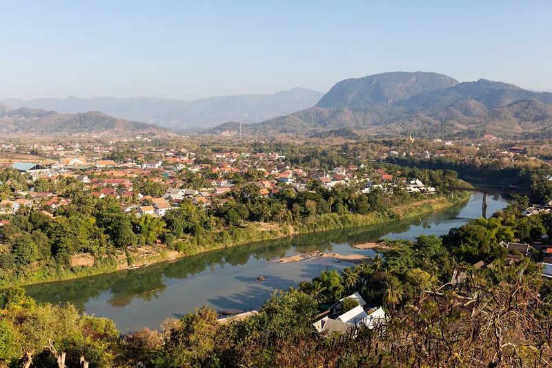 Aerial view of Luang Prabang town along the Nam Khan River, surrounded by mountains, seen from Mount Phousi.